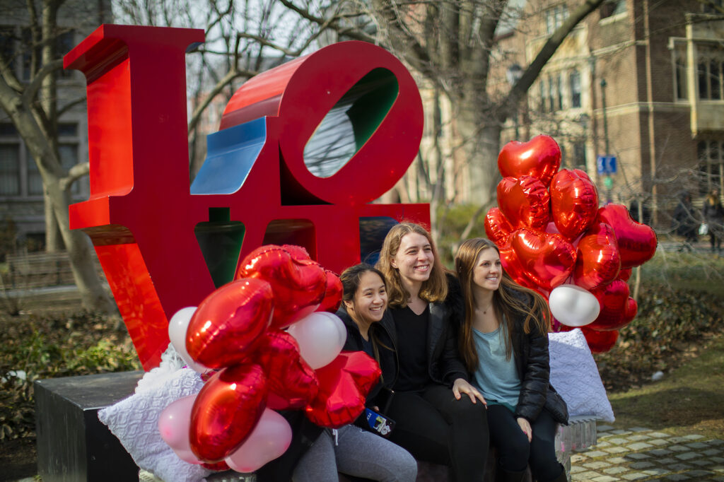 students sit in front of LOVE sculpture